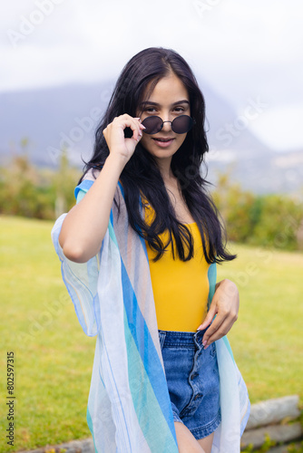 Young biracial woman lowering sunglasses, standing outdoors at home