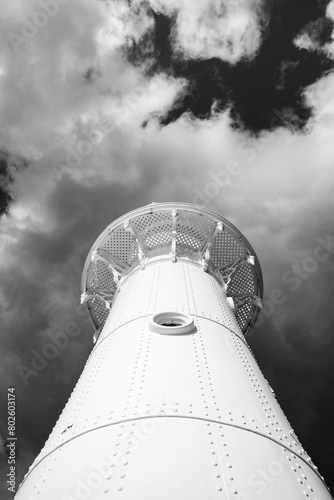 Looking up to the head of a lighthouse under a mood filled cloudy sky in monochrome