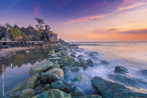 clean sea water and lots of rocks lined up near the sea water and misty sunset nuances with purplish and yellowish colors at Pura Batu Bolong Lombok