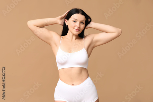 Body positive woman in underwear smiling on beige background