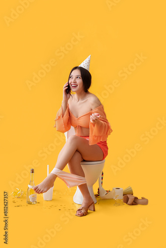 Young Asian woman talking by mobile phone on toilet bowl after party against ...