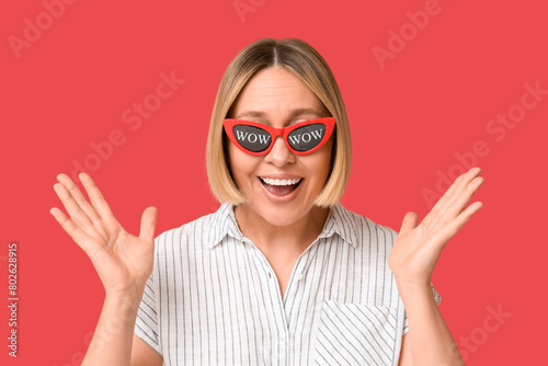 Surprised adult woman in eyeglasses with words WOW on red background