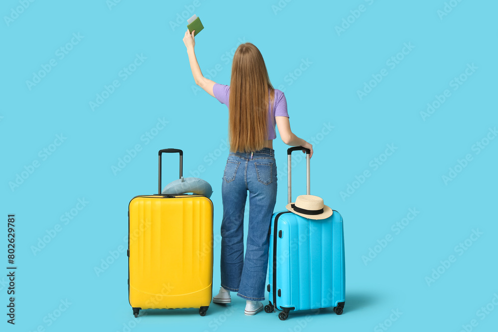 Young woman with suitcases, raising up her hand with passport on blue background. Travel concept. Back view Young woman with suitcases, raising up her hand with passport on blue background. Travel concept. Back view