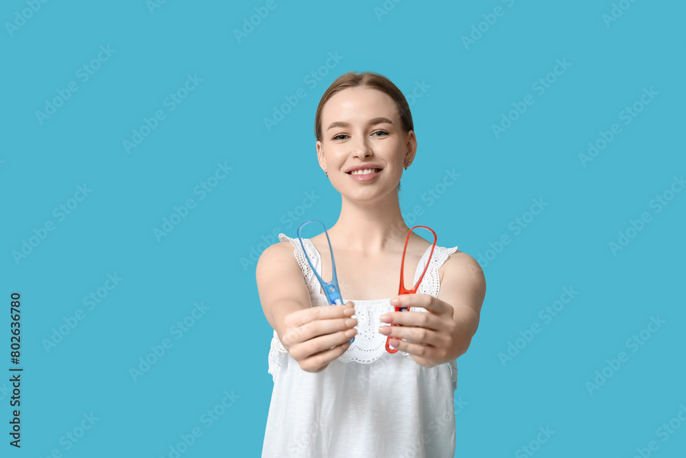 Young woman with tongue scrapers on blue background Young woman with tongue scrapers on blue background