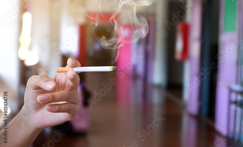 Hand holding lighted cigarette with smoking in front hallway of secondary school, concept for smoking problems in educational area. photo