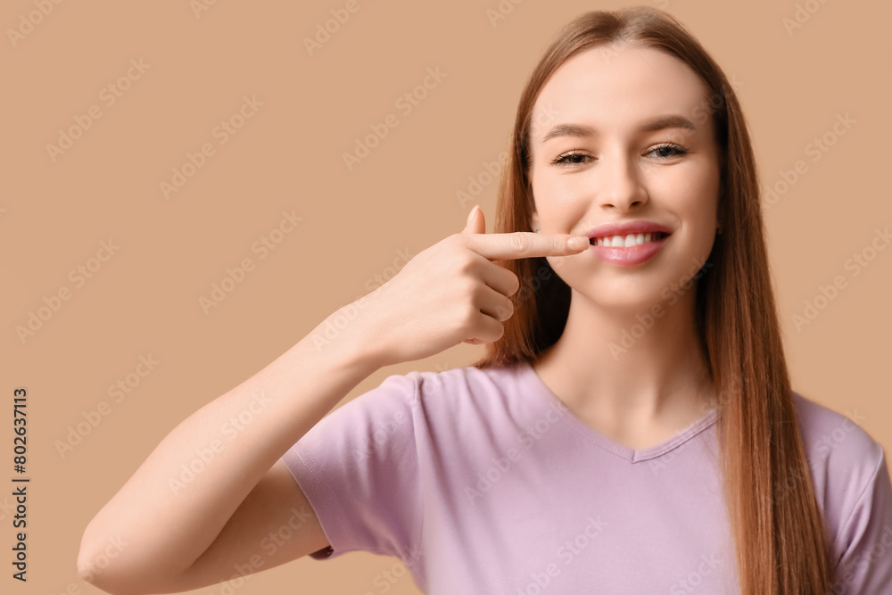 Young woman pointing at her teeth on beige background Young woman pointing at her teeth on beige background