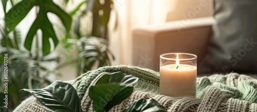 Simple arrangement featuring green tropical foliage, a lit candle, and a stylish cozy sweater. Scandinavian-inspired decor with Nordic elements in a modern interior setting.
