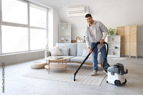 Young bearded man cleaning carpet at home