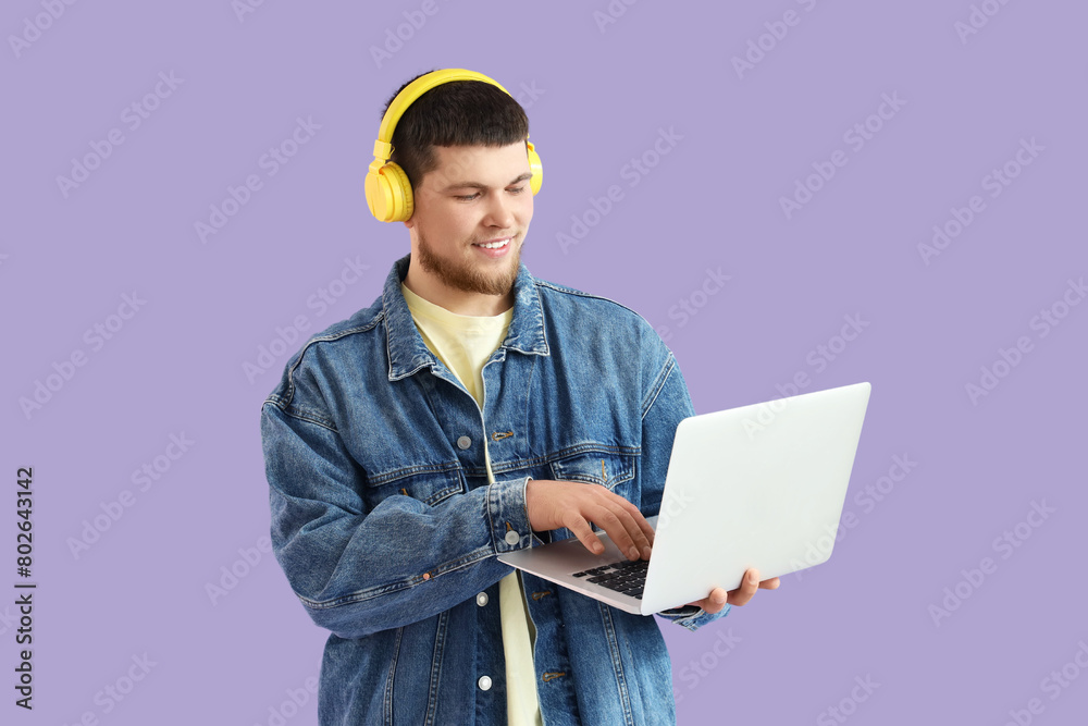 Young bearded man in headphones using laptop on lilac background Young bearded man in headphones using laptop on lilac background