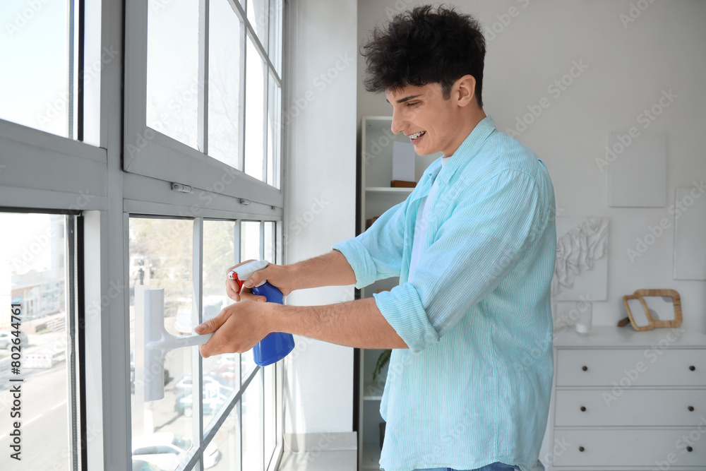 Young man cleaning window with squeegee at home