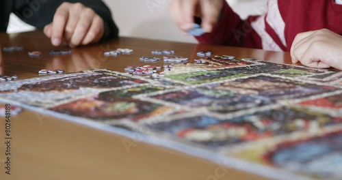 Two boys engage in teamwork as they focus on assembling a colorful jigsaw puzzle on a wooden table, their hands carefully selecting pieces.