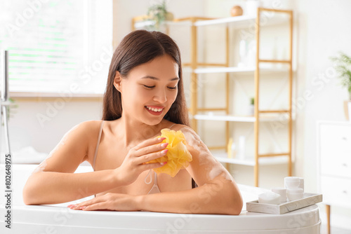 Young Asian woman with loofah and soap taking bath at home