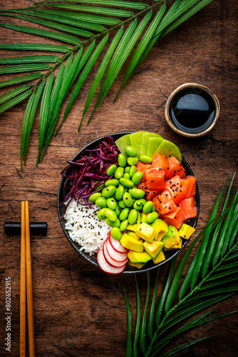 Poke bowl for balanced diet with salmon, avocado, radish, cabbage, beans, sesame and rice, wooden table background, top view