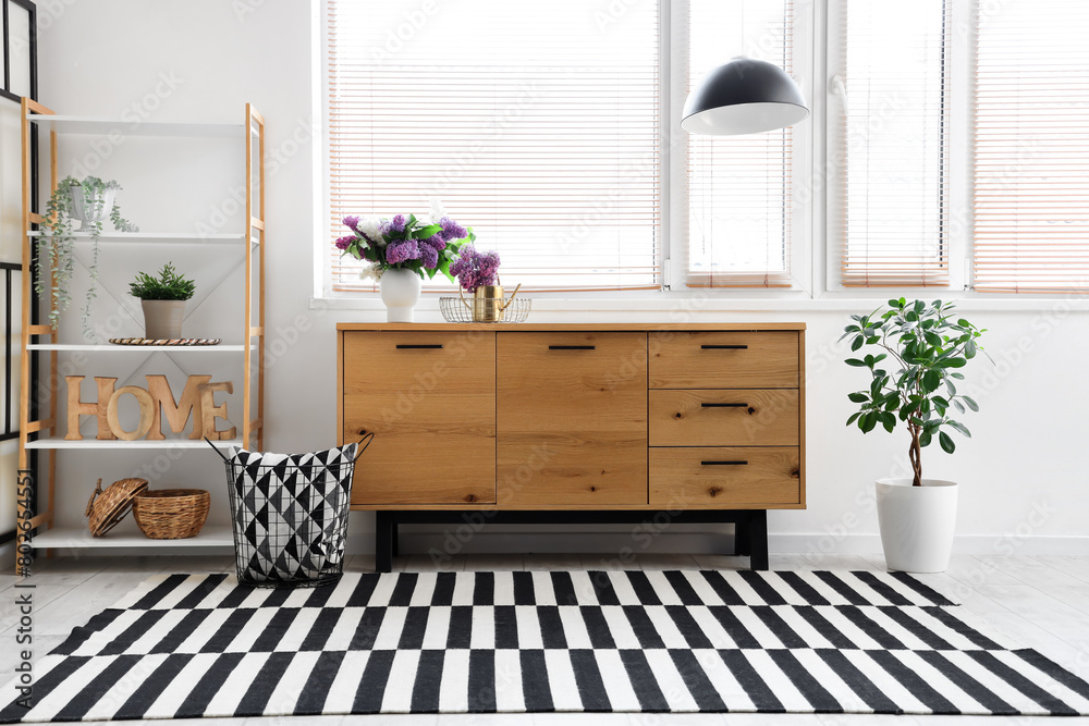Stylish wooden cabinet and shelving unit near window in light room Stylish wooden cabinet and shelving unit near window in light room