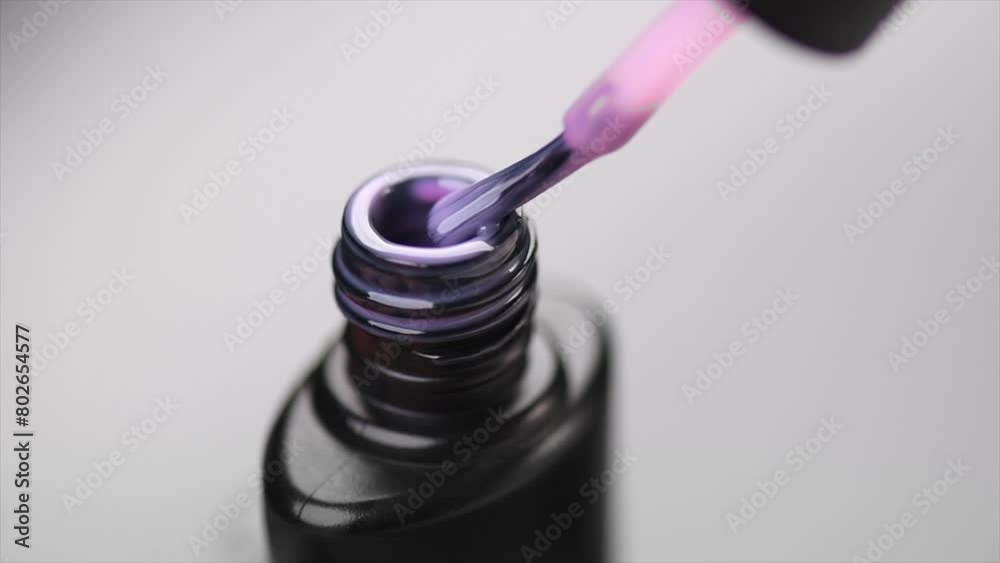Gel nail polish, pink shellac UV gel bottle, brush, varnish, manicure concept, slow motion. Manicure salon. Black bottle over gray background, close up. Gel nail polish, pink shellac UV gel bottle, brush, varnish, manicure concept, slow motion. Manicure salon. Black bottle over gray background, close up.