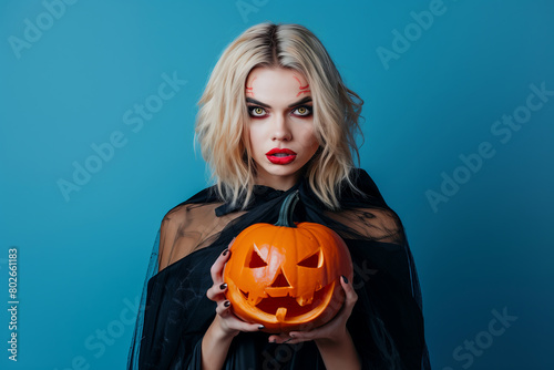 Woman with white makeup and red face paint holding a carved pumpkin, styled for Halloween makeup fashion and beauty modeling