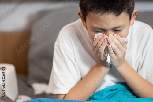 Sick child boy having allergies,hay fever,runny nose,sneezing,nasal congestion,blow the nose with tissue paper,inflammation of a nasal sinus,allergic rhinitis,seasonal allergy or dust,air pollution