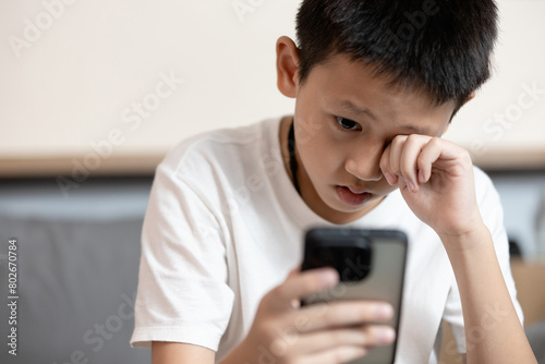 Asian child boy overusing his smart phone,addicted to mobile phone,game addiction,effects on young children's brains,disease of ADHD,Nomophobia,dry eyes,eyesight problems,loss of vision,health care