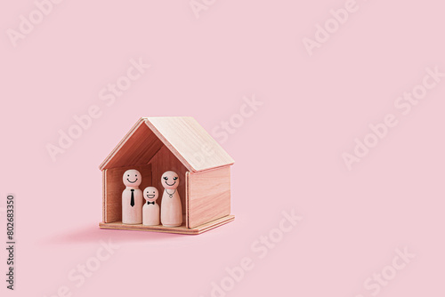 Happy wooden family figures inside a tiny wooden house isolated on a pink background. Parent and smiling kid stand close together