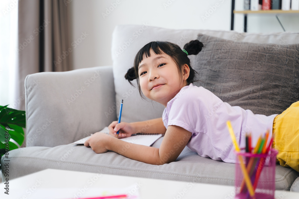 A young girl is sitting on a couch with a pencil and a notebook A young girl is sitting on a couch with a pencil and a notebook