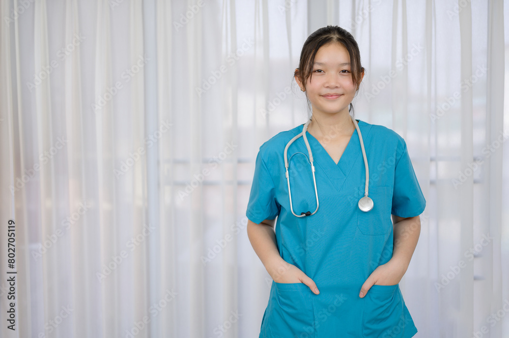 Young female nurse or medical assistant with Asian stethoscope Wear a green nurse's uniform Happy smiling man standing by the window during a break from work at a medical clinic or hospital. Young female nurse or medical assistant with Asian stethoscope Wear a green nurse's uniform Happy smiling man standing by the window during a break from work at a medical clinic or hospital.