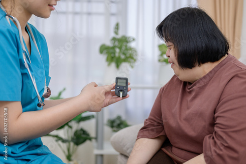 A young Asian nurse uses a glucometer to test her blood sugar level to test diabetes in a disabled Asian woman with Down syndrome.