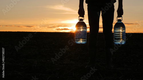 A man holds two bottles of drinking water, stands in a field at sunset