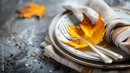 Plate with cutlery napkin and autumn leaf on table