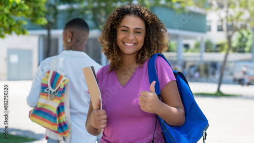 Successful hispanic female student with backpack and paperwork infront of university