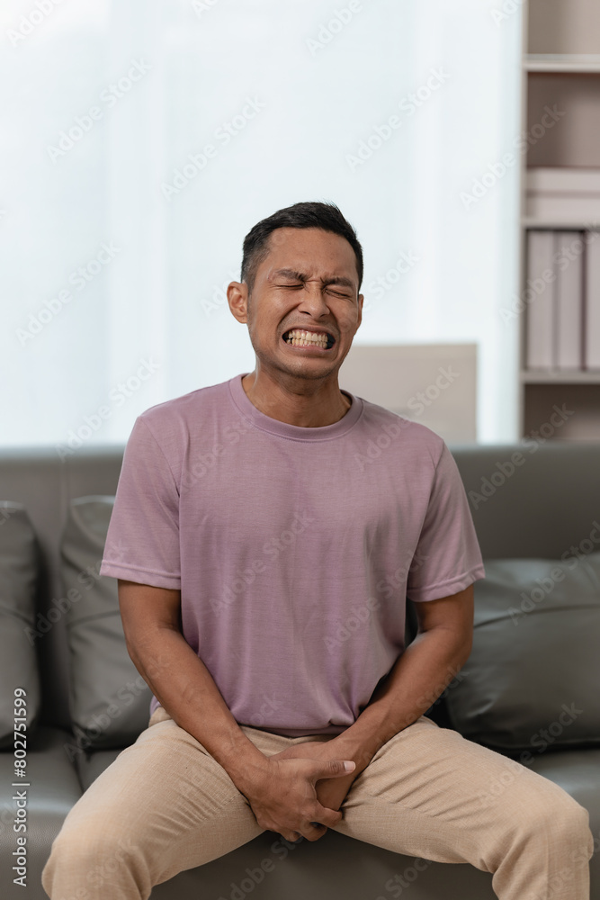 A man is sitting on a sofa and touching his crotch. The concept of holding back pee, missing the bathroom, prostate cancer, UTI or urinary tract infection.