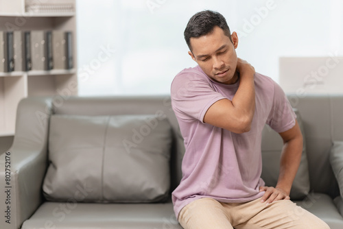 Asian man with back pain Massaging sore muscles while sitting on the sofa, elderly people and health problems concept.