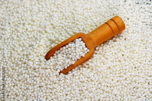 White sago pearls in a wooden scoop on a sago background.