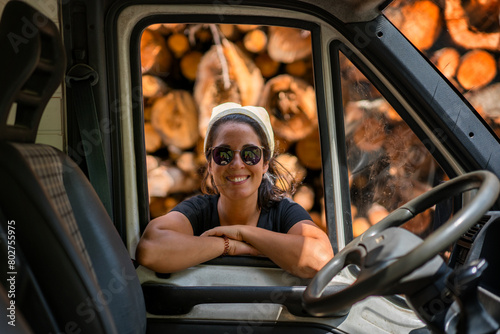 Woman looking through a car window with wood logs behind her photo
