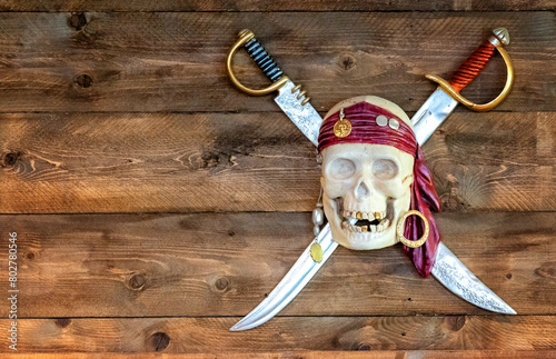 Jolly pirate scull in bandanna with crossed swords and golden teeth on wooden background. photo