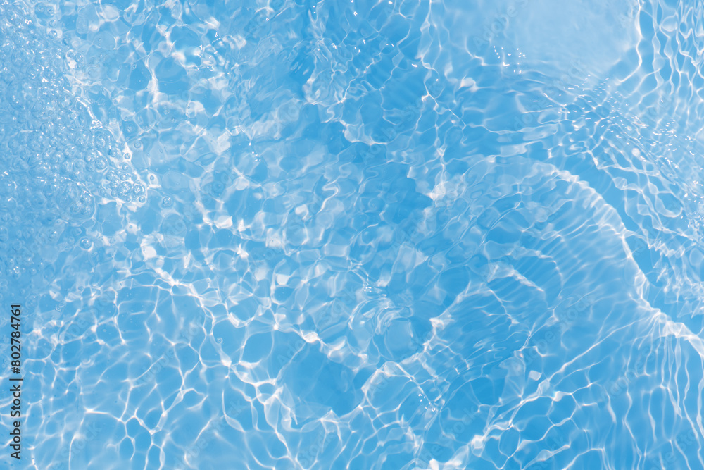 Obraz premium Blue water with ripples on the surface. Defocus blurred transparent blue colored clear calm water surface texture with splashes and bubbles. Water waves with shining pattern texture background.