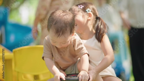 Two asian little siblings playing together at outdoor playground sitting on the 4 wheels bikes, older sister teasing her toddler little brother, family love bonding, children emotions and habits