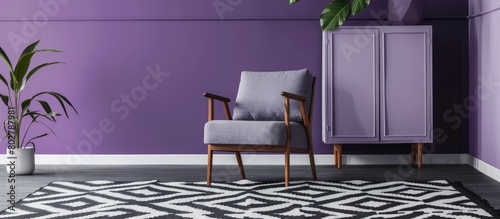 Actual image of a grey wooden armchair placed on a patterned black and white rug in an artistic living room setting featuring a geometric violet wall and cabinet. photo