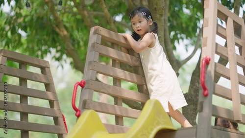 Active asian little girl playing inside sunny park during day, sliding down from playground yellow slider. Child Movement. Leisure Activity. Kid playtime learning development, Childhood experience