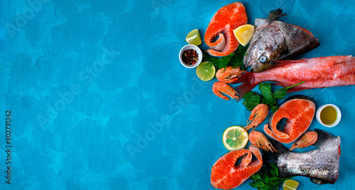 Fresh seafood assortment on blue background with copy space. Trout steaks, beaked redfish and shrimps.  Cooking ingredients. Top view