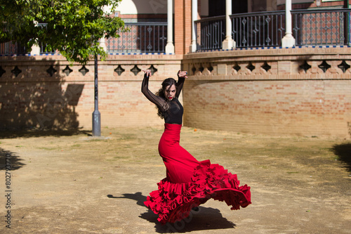 Beautiful woman dancing flamenco in Seville, Spain. She wears a red and black dress typical of a flamenco dancer with a lot of art, you can see the movement in the air of the frilly dress.