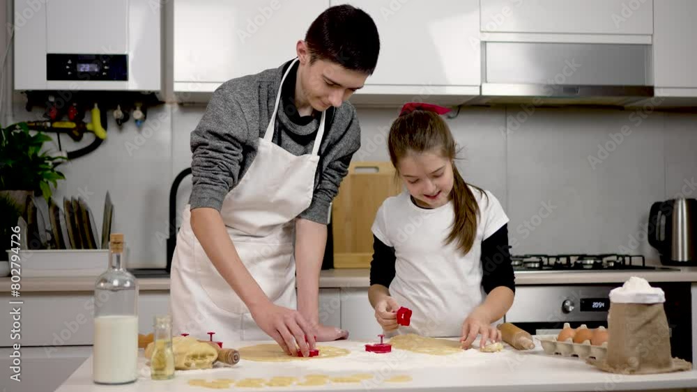 Boy and girl wearing apron cutting dough with cookie cutter in cozy kitchen. Children making cakes. Kids study. Homeschooling. Happy brother and sister independently prepare culinary surprise from Boy and girl wearing apron cutting dough with cookie cutter in cozy kitchen. Children making cakes. Kids study. Homeschooling. Happy brother and sister independently prepare culinary surprise from