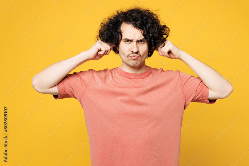 Young sad dissatisfied man he wear pink t-shirt casual clothes cover ears with hands fingers do not want to listen scream isolated on plain yellow orange background studio portrait. Lifestyle concept. Young sad dissatisfied man he wear pink t-shirt casual clothes cover ears with hands fingers do not want to listen scream isolated on plain yellow orange background studio portrait. Lifestyle concept.