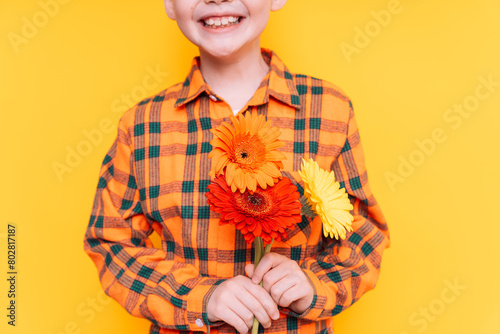 Boy in a shirt holding flowers in his hands against a yellow background.