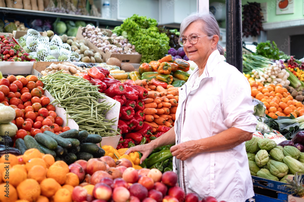 Senior woman buying fresh fruit and vegetables at the market, choosing from a large selection. Healthy eating, the concept of spending and consumerism