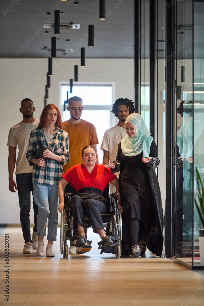 Fototapeta premium A diverse group of young business people walking a corridor in the glass-enclosed office of a modern startup, including a person in a wheelchair and a woman wearing a hijab