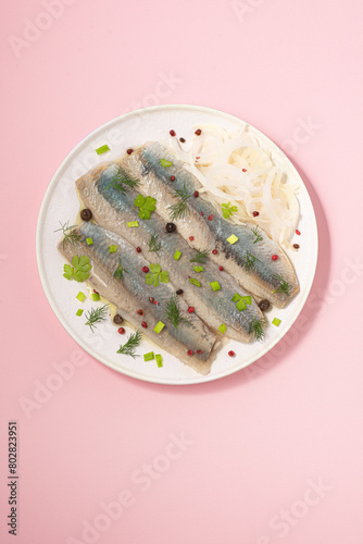Spicy salted herring with pepper served with pickled onions. An important fish, the first ingredient of Scandinavian and Baltic cuisine, traditional preservation. Baltic herring. Pink soft background.
