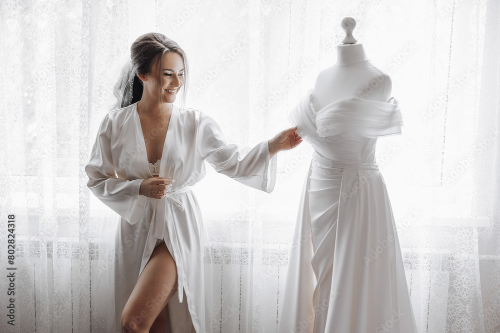 A bride is standing in front of a wedding dress, smiling. The dress is white and has a long train A bride is standing in front of a wedding dress, smiling. The dress is white and has a long train