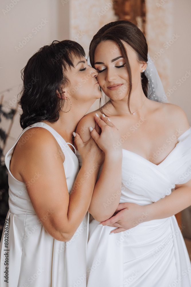 Two women are hugging each other, one of them is wearing a wedding dress. Scene is warm and affectionate