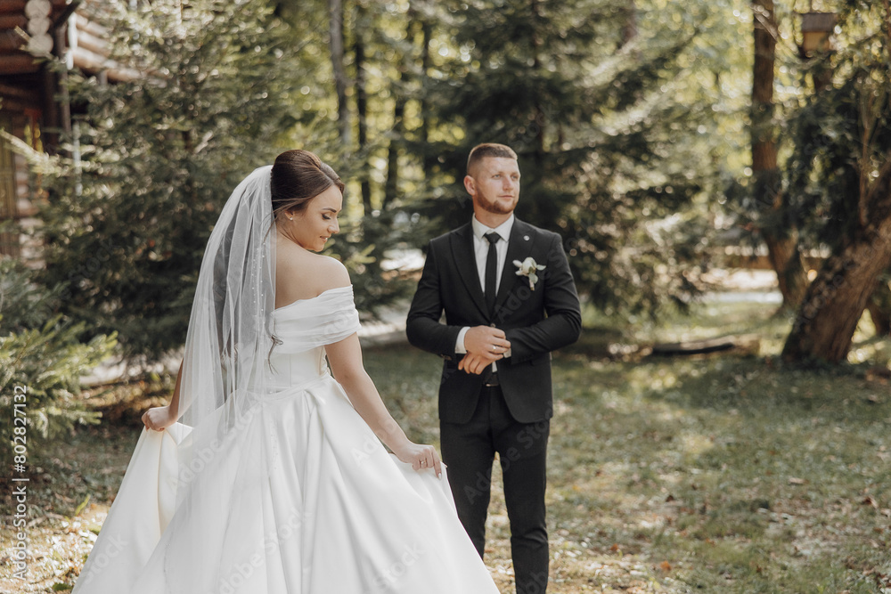 A bride and groom stand in a forest clearing, with the bride wearing a white dress and the groom wearing a black suit A bride and groom stand in a forest clearing, with the bride wearing a white dress and the groom wearing a black suit