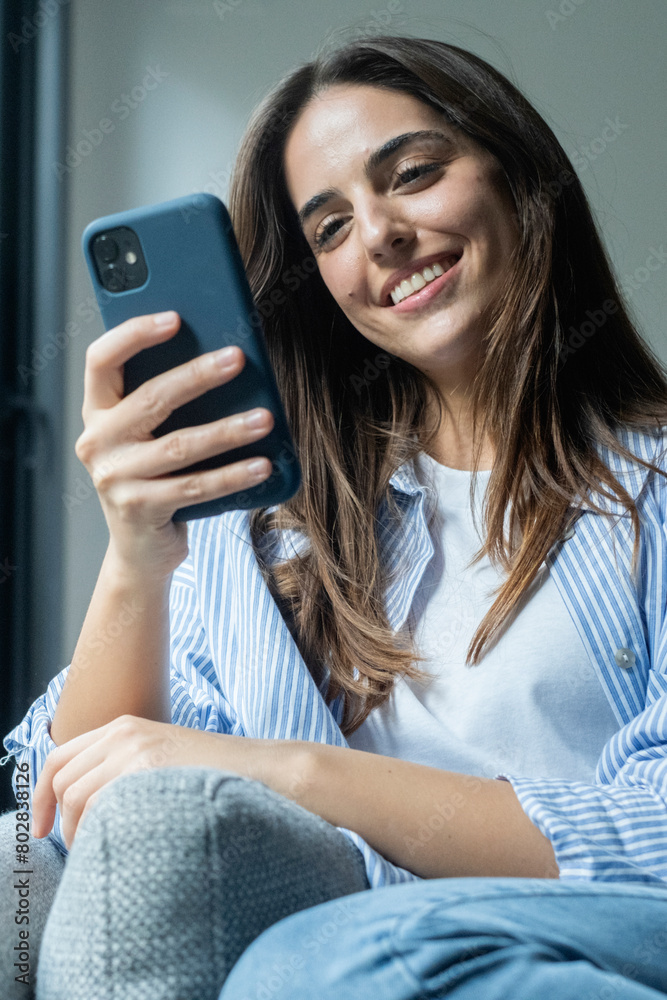 Happy pleasant millennial woman relaxing on comfortable couch, holding smartphone in hands. Smiling young lady chatting in social networks, watching funny videos, using mobile applications at home. Happy pleasant millennial woman relaxing on comfortable couch, holding smartphone in hands. Smiling young lady chatting in social networks, watching funny videos, using mobile applications at home.